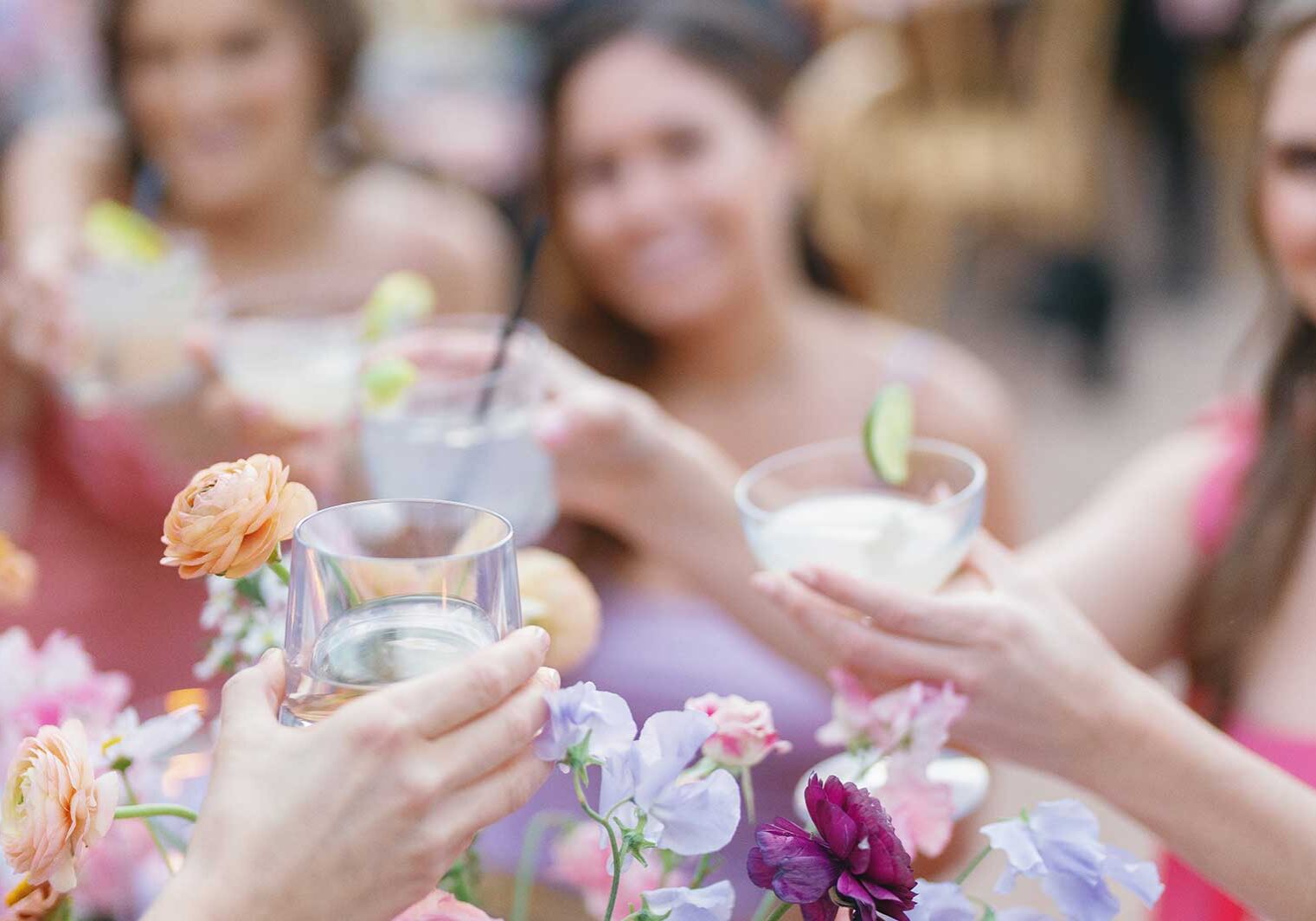 Three focused hands holding drinks with girls blurred in the background